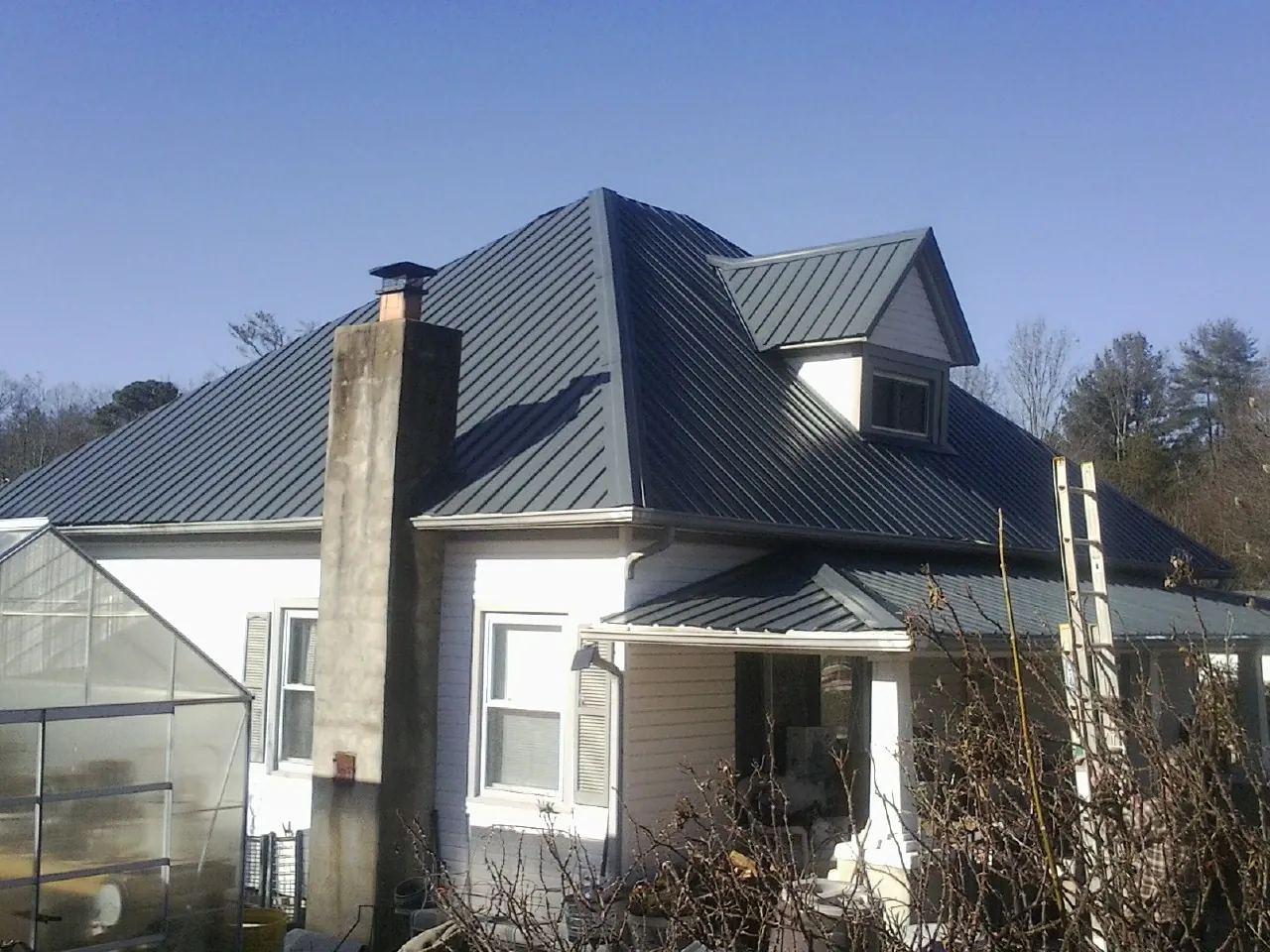 Dark blue standing seam metal roof on a white farmhouse with dormer — Slate & Tile Roof Repair by Roofing Brothers in Westerly