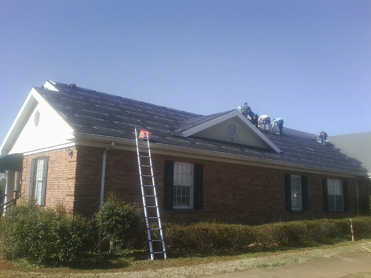 Crew tearing shingles off a brick ranch roof with a ladder set — Emergency Roof Repair work by our crew in Westerly