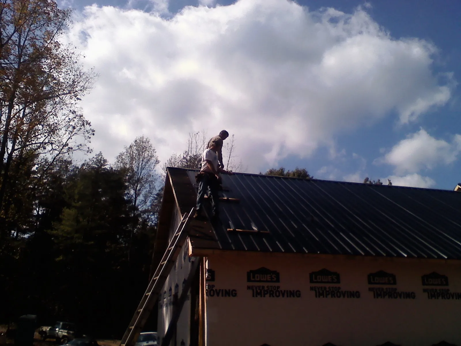 Roofer fastening dark metal panels high against a cloudy sky, from a Roof Inspection job in Westerly